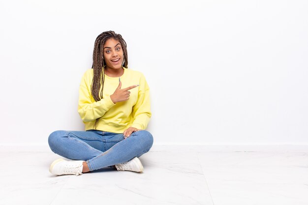 Jovem afro parecendo animada e surpresa, apontando para o lado