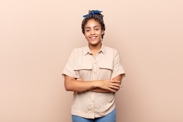 Jovem afro parecendo uma empreendedora feliz, orgulhosa e satisfeita, sorrindo com os braços cruzados