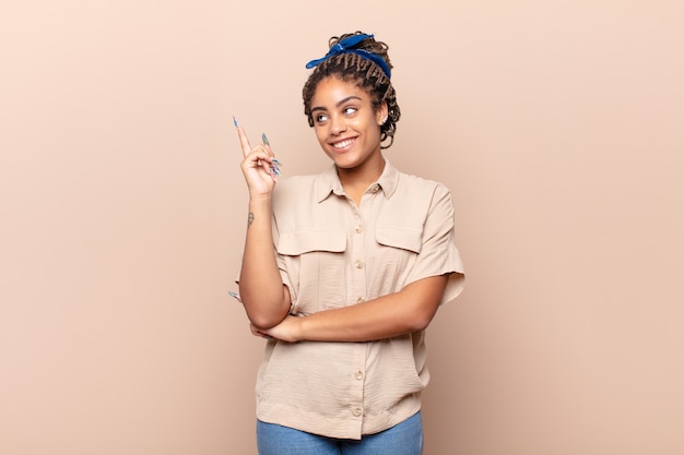 Jovem afro sorrindo feliz e olhando de soslaio, pensando, pensando ou tendo uma ideia