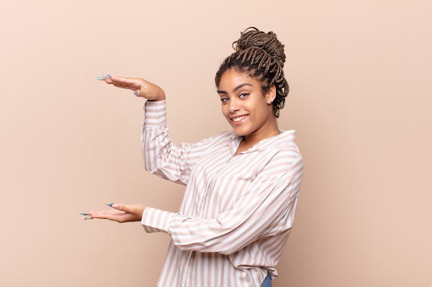 Jovem afro sorrindo, sentindo-se feliz, positiva e satisfeita, segurando o objeto