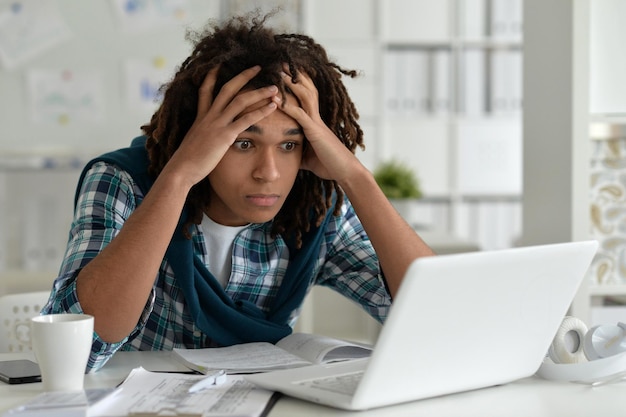 Foto jovem afro trabalhando no escritório, usando laptop