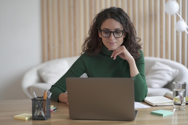 Jovem agradável freelancer italiana trabalhando em laptop remotamente de casa atraente mulher espanhola em óculos estudando on-line ou fazendo compras na loja de internet Conceito freelance