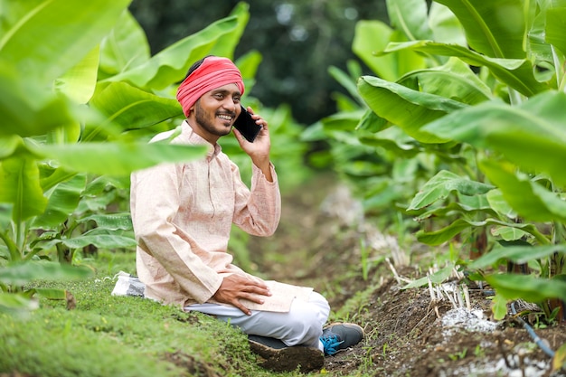 Jovem agricultor indiano falando em smartphone no campo de agricultura de banana.