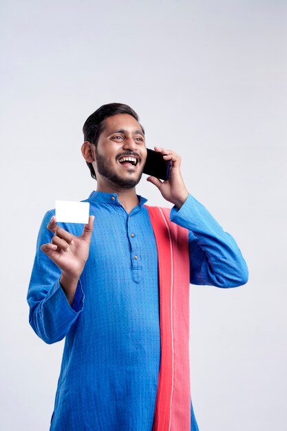 Jovem agricultor indiano mostrando cartão e falando no celular sobre fundo branco