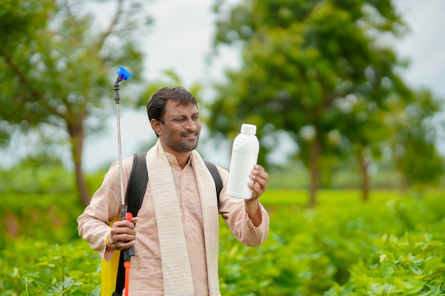 Jovem agricultor indiano mostrando o frasco de fertilizante líquido no campo de agricultura.