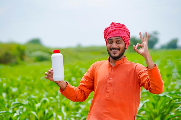 Jovem agricultor indiano mostrando o frasco de fertilizante líquido no campo de agricultura.