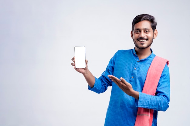 Jovem agricultor indiano mostrando smartphone e dando expressão em fundo branco.