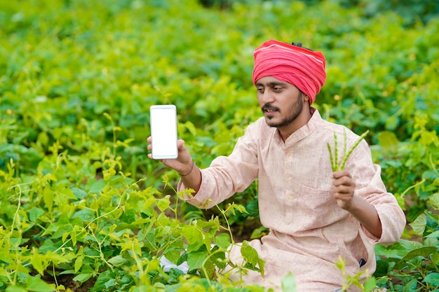 Jovem agricultor indiano mostrando smartphone no campo de agricultura.