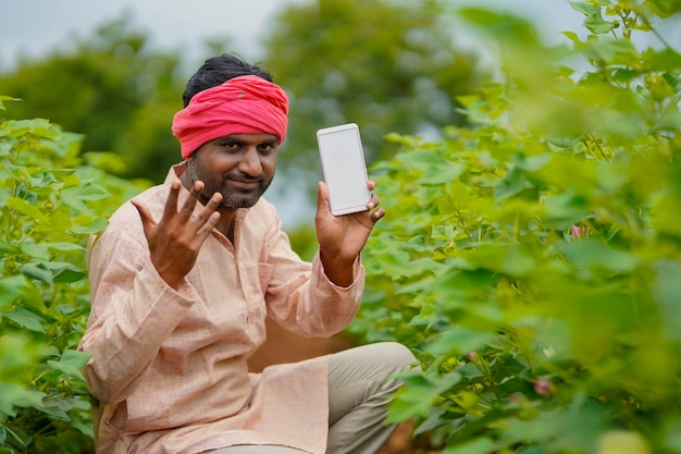 Jovem agricultor indiano mostrando smartphone no campo de agricultura.