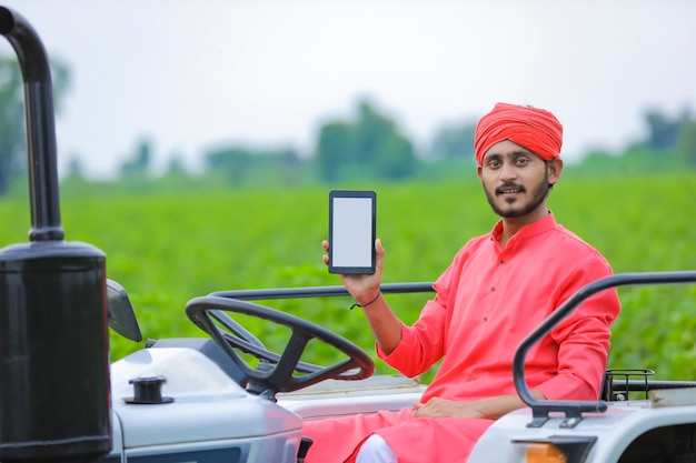 Jovem agricultor indiano mostrando smartphone ou tablet no campo agrícola