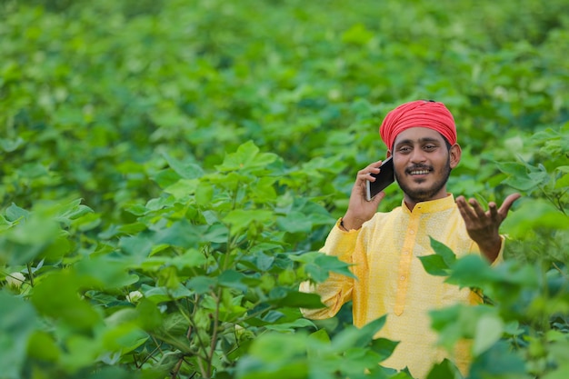 Jovem agricultor indiano ou trabalhador falando ao telefone celular em um campo de algodão