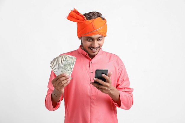 Jovem agricultor indiano usando smartphone e mostrando dinheiro em fundo branco.