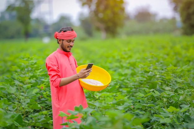 Jovem agricultor indiano usando smartphone em um campo de algodão verde