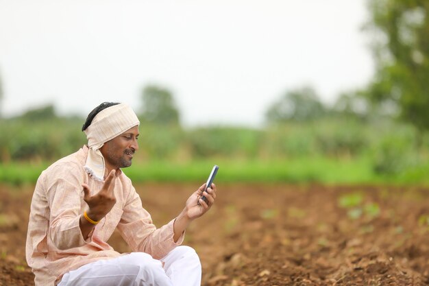 Jovem agricultor indiano usando smartphone no campo de agricultura.