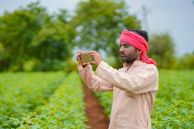 Jovem agricultor indiano usando smartphone no campo de agricultura.