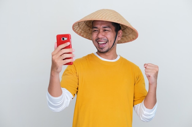 Jovem agricultor indonésio sorrindo animado ao olhar para seu handphone