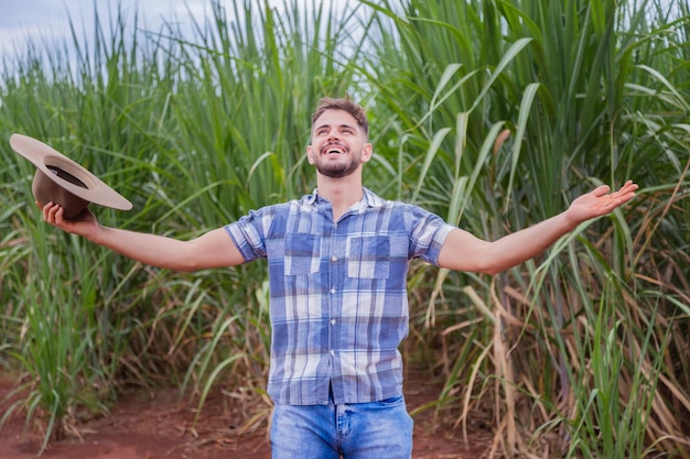 Jovem agricultor latino trabalhando na plantação de cana-de-açúcar Agricultor brasileiro Agricultor brasileiro de braços abertos feliz em um campo de cana-de-açúcar