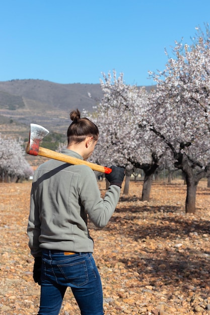 Jovem agricultor moderno com machado em seu campo de árvore de ombro ao fundo