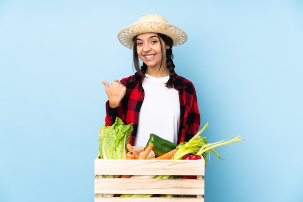 Jovem agricultor Mulher segurando legumes frescos em uma cesta de madeira, apontando para o lado para apresentar um produto