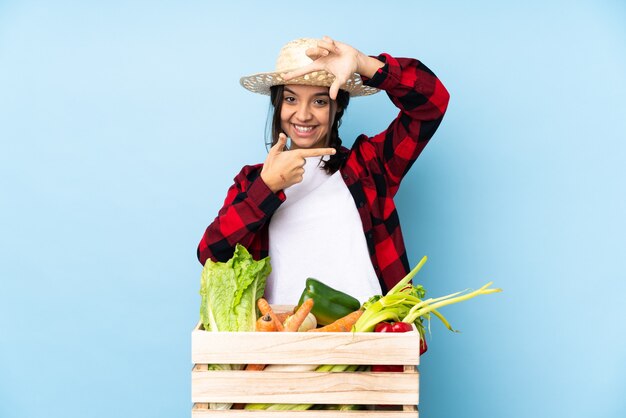 Jovem agricultor mulher segurando legumes frescos em uma cesta de madeira com foco no rosto. símbolo de enquadramento