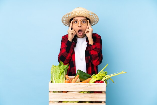 Jovem agricultor Mulher segurando legumes frescos em uma cesta de madeira com óculos e surpresa