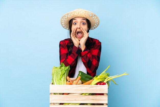 Jovem agricultor Mulher segurando legumes frescos em uma cesta de madeira, gritando e anunciando algo