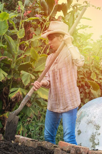 Jovem agricultora com chapéu e pá na mão trabalhando a terra