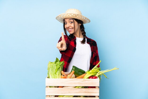 Jovem agricultora Mulher segurando legumes frescos em uma cesta de madeira, mostrando e levantando um dedo
