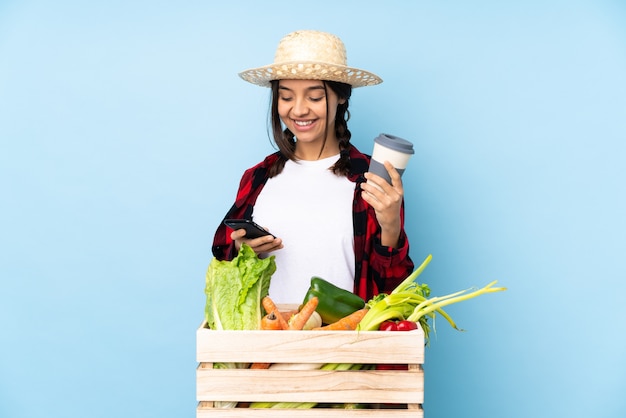 Jovem agricultora Mulher segurando legumes frescos em uma cesta de madeira segurando café para levar e um móbile