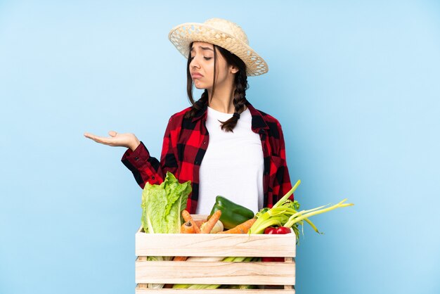 Jovem agricultora Mulher segurando legumes frescos em uma cesta de madeira segurando copyspace com dúvidas