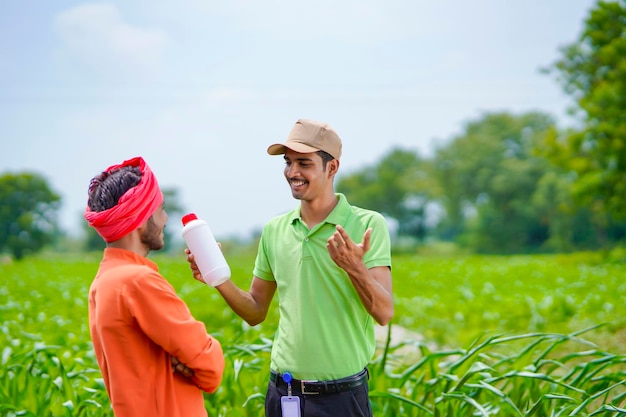 Jovem agrônomo indiano dando frasco de fertilizante líquido ao agricultor no campo de agricultura verde.