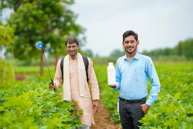 Jovem agrônomo indiano dando uma garrafa de fertilizante líquido ao agricultor e dizendo informações sobre o produto no campo de agricultura verde.