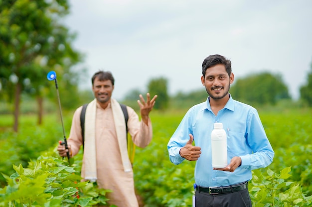 Jovem agrônomo indiano dando uma garrafa de fertilizante líquido ao agricultor e dizendo informações sobre o produto no campo de agricultura verde.