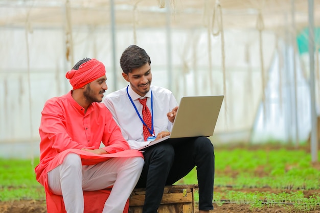 Jovem agrônomo indiano mostrando algumas informações ao agricultor em um laptop em uma estufa