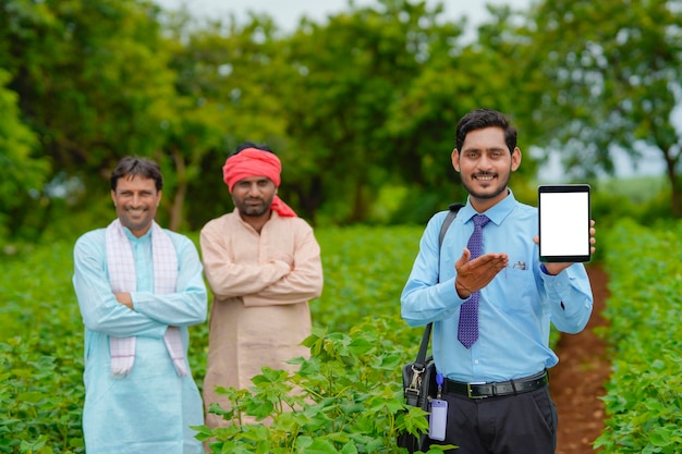 Jovem agrônomo indiano ou banqueiro mostrando tablet com agricultores no campo de agricultura.