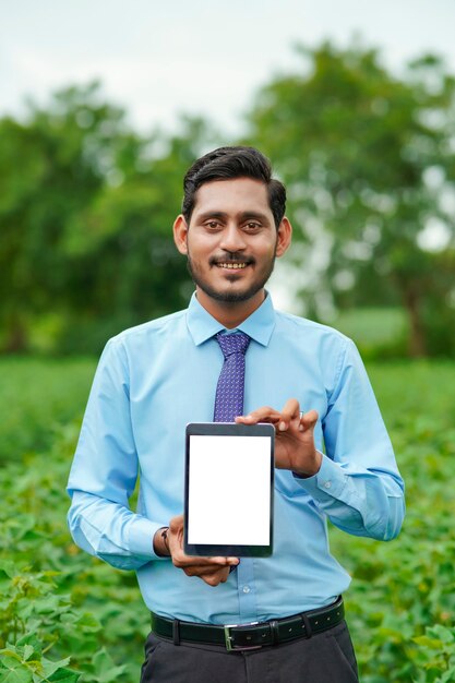 Jovem agrônomo indiano ou oficial mostrando o tablet no campo de agricultura.