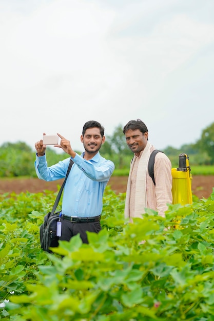 Jovem agrônomo ou banqueiro indiano, mostrando algumas informações ao agricultor no smartphone no campo da agricultura.