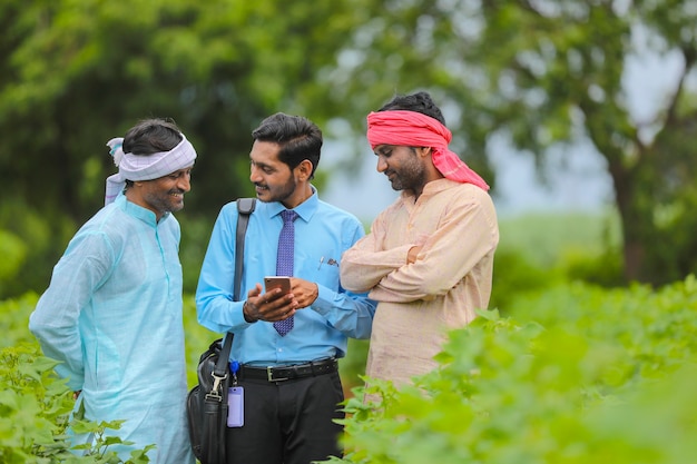 Jovem agrônomo ou banqueiro indiano, mostrando algumas informações ao agricultor no smartphone no campo da agricultura.