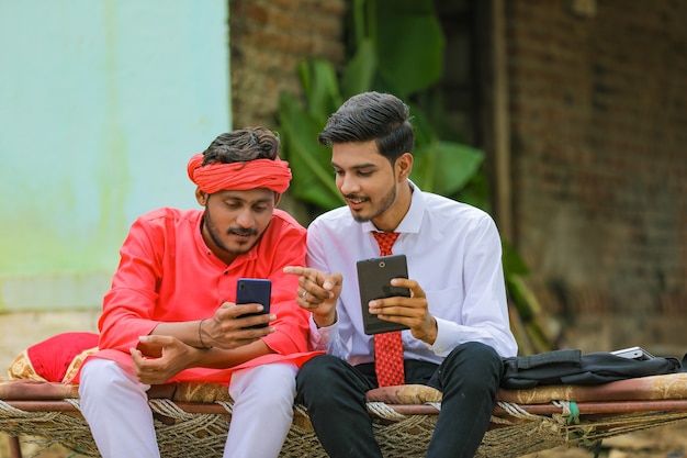 Jovem agrônomo ou banqueiro indiano mostrando algumas informações ao agricultor no smartphone