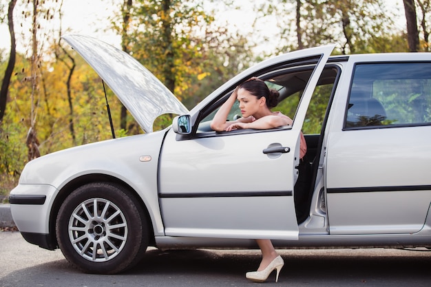 Foto jovem aguarda assistência perto de seu carro, que quebrou na beira da estrada