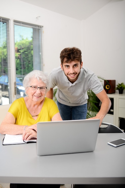 Jovem ajudando uma velha idosa cuidando da papelada e dos procedimentos administrativos com o laptop em casa