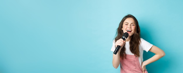 Jovem alegre cantando karaokê segurando microfone e sorrindo se divertindo em pé sobre ba azul