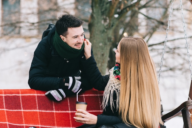 Jovem alegre casal apaixonado está bebendo café no inverno ao ar livre. Eles estão sorrindo e olhando um para o outro durante um encontro romântico