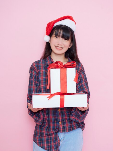 Jovem alegre com chapéu de Papai Noel segurando caixas de presente no fundo rosa