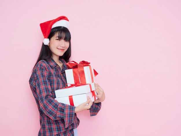 Jovem alegre com chapéu de Papai Noel segurando caixas de presente no fundo rosa