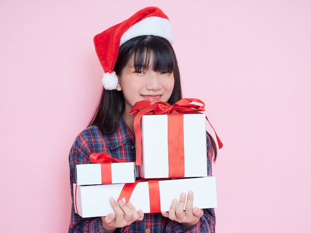 Jovem alegre com chapéu de Papai Noel segurando caixas de presente no fundo rosa