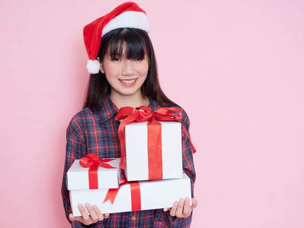 Jovem alegre com chapéu de Papai Noel segurando caixas de presente no fundo rosa