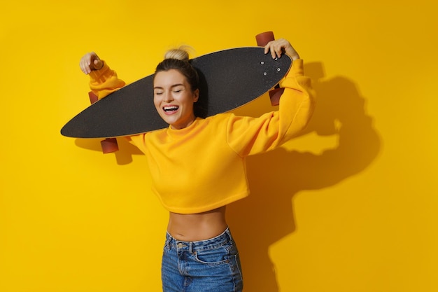 Jovem alegre com longboard contra fundo amarelo