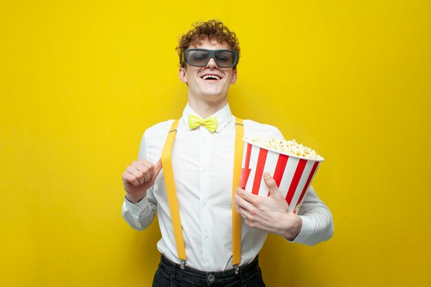 Foto jovem alegre com roupa festiva em óculos 3d assiste filme com pipoca em fundo amarelo