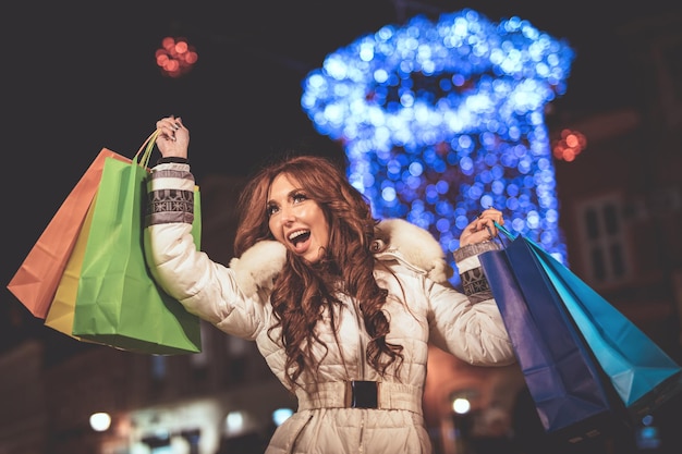 Jovem alegre com sacolas coloridas se divertindo na rua da cidade na época do Natal.